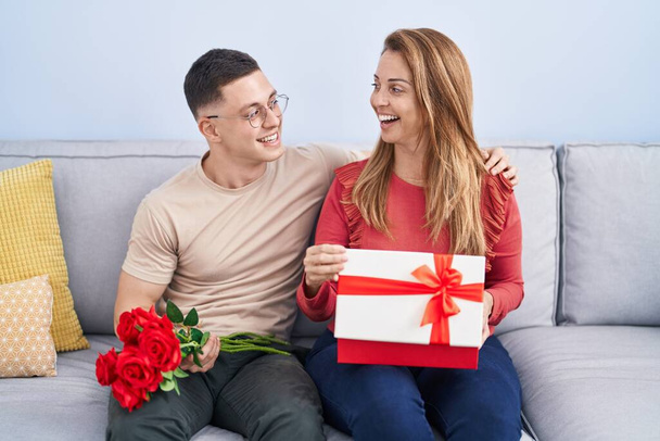 Чоловік і жінка мати і син тримають подарунок і квіти вдома
 - Фото, зображення