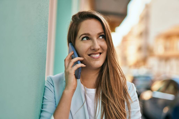 Giovane donna d'affari bionda sorridente felice parlando sullo smartphone in città. - Foto, immagini