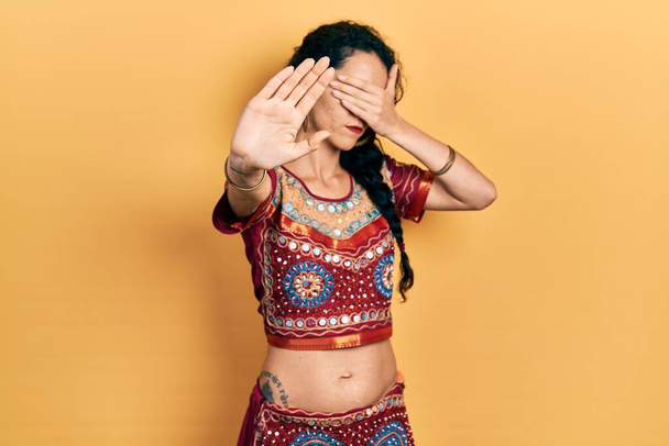 Молодая женщина в бинди и болливудской одежде закрывает глаза руками и делает остановку жеста с грустным и испуганным выражением. смущенная и негативная концепция.  - Фото, изображение