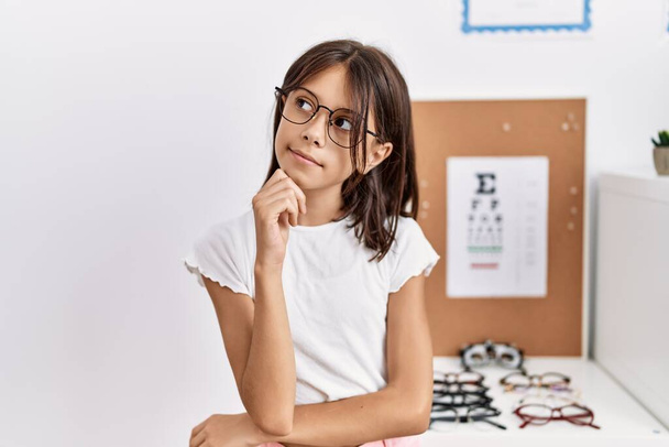Young hispanic girl wearing glasses with hand on chin thinking about question, pensive expression. smiling with thoughtful face. doubt concept.  - Zdjęcie, obraz
