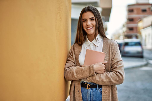 Junge hispanische Studentin lächelt glücklich und hält Buch in der Hand. - Foto, Bild