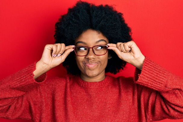 Молода афро-американська жінка в окулярах посміхається дивлячись збоку і дивлячись геть думки.  - Фото, зображення