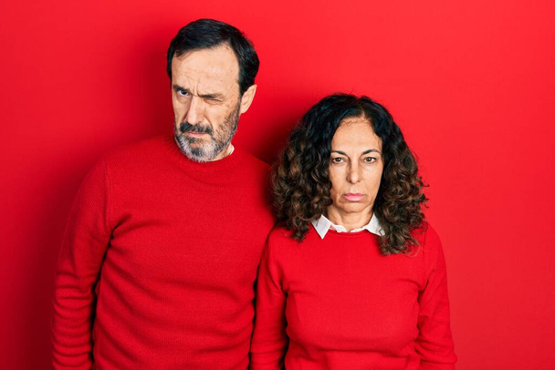 Μεσήλικες ζευγάρι Ισπανίδα γυναίκα και ο άνθρωπος αγκαλιάζει και στέκεται μαζί σκεπτικιστής και νευρικός, συνοφρυωμένος αναστατωμένος λόγω του προβλήματος. αρνητικό πρόσωπο.  - Φωτογραφία, εικόνα