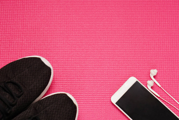 Вид сверху смартфона в наушниках и на красном коврике Yoga. Фитнес и здоровая концепция с копировальным пространством. - Фото, изображение