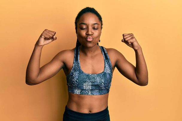 African american woman with braided hair wearing sportswear showing arm muscles looking at the camera blowing a kiss being lovely and sexy. love expression.  - Foto, Imagen