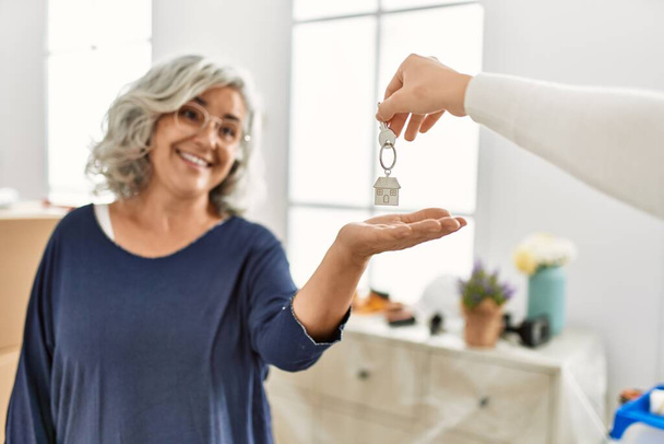 Grauhaarige Frau mittleren Alters lächelt glücklich und hält Schlüssel für neues Zuhause in der Hand. - Foto, Bild