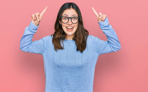 Young beautiful woman wearing casual clothes and glasses smiling amazed and surprised and pointing up with fingers and raised arms.  - Фото, изображение
