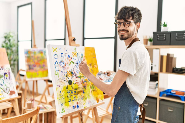 Fiatal spanyol művész férfi mosolyog boldog rajz a művészeti stúdióban. - Fotó, kép