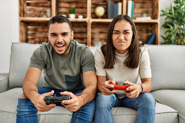 Νεαρό ζευγάρι Λατίνων απογοητευμένο παίζοντας βιντεοπαιχνίδι στο σπίτι. - Φωτογραφία, εικόνα
