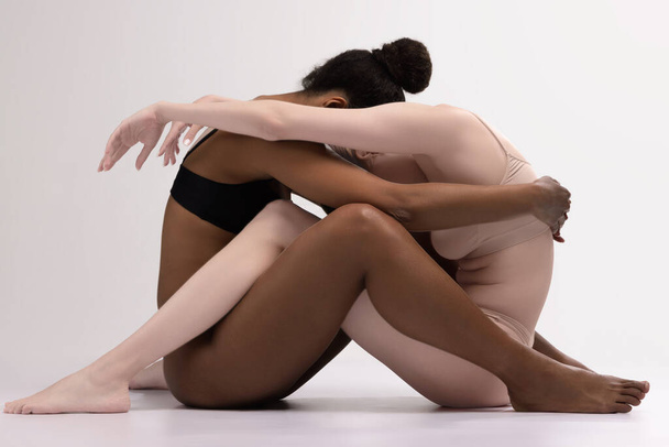 Love and support. Conceptual portrait of two different women sitting and hugging isolated on white background. Concept of friendship, pride, unity, queer. Human rights, choice and equality - Fotoğraf, Görsel
