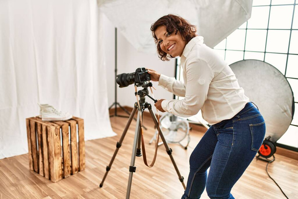 Młoda latynoska fotograf kobieta uśmiechnięta szczęśliwy za pomocą kamery w studio fotograficznym. - Zdjęcie, obraz
