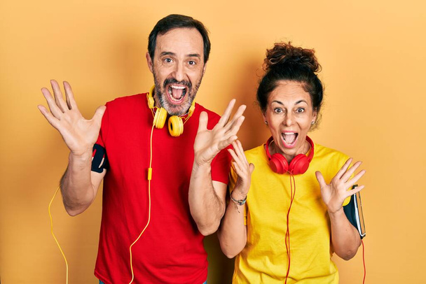 Middle age couple of hispanic woman and man wearing sportswear and arm band celebrating crazy and amazed for success with arms raised and open eyes screaming excited. winner concept  - Photo, Image