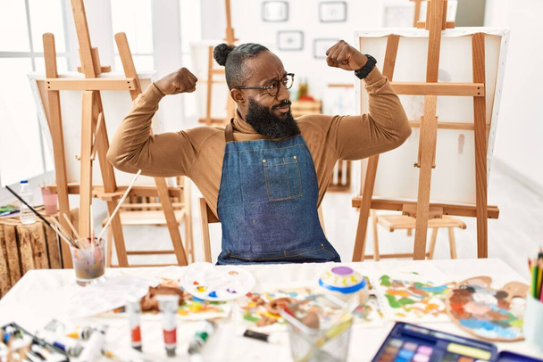 Artista afro-americano homem no estúdio de arte mostrando músculos braços sorrindo orgulhoso. conceito de aptidão.  - Foto, Imagem