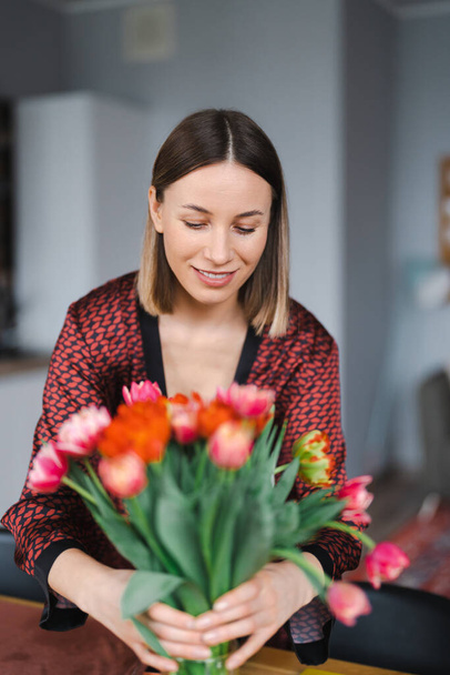 Mooie vrouw arrangeren bloemen gepresenteerd door haar man thuis, gelukkig en vrolijk - Foto, afbeelding