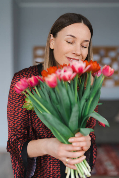 Happy woman enjoy bouquet of tulips. Housewife enjoying a bunch of flowers and interior of kitchen. Sweet home. Allergy free - Фото, изображение