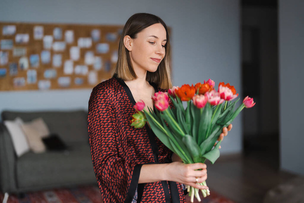 Happy woman enjoy bouquet of tulips. Housewife enjoying a bunch of flowers and interior of kitchen. Sweet home. Allergy free - Photo, Image