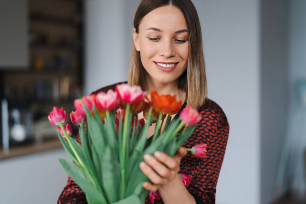Mujer feliz disfrutar de ramo de tulipanes. Ama de casa disfrutando de un ramo de flores y el interior de la cocina. Dulce hogar. Libre de alergia - Foto, imagen