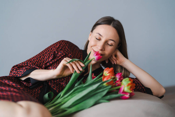 Happy woman enjoy bouquet of tulips. Housewife enjoying a bunch of flowers while relaxing on a comfy bean bag. Sweet home. Allergy free - Photo, image