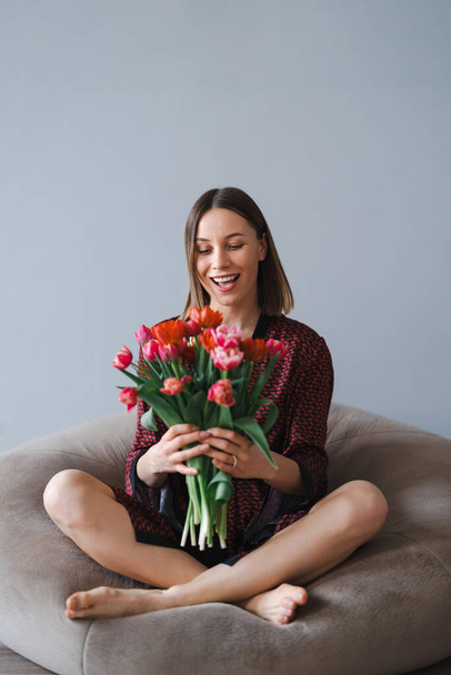 Szczęśliwa kobieta lubi bukiet tulipanów. Gospodyni domowa ciesząca się bukietem kwiatów relaksując się na wygodnej torebce z fasolą. Słodki dom. Wolne od alergii - Zdjęcie, obraz