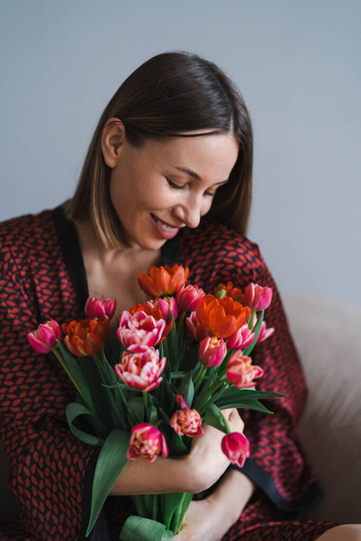 Boldog nő élvezi a tulipán csokrot. Háziasszony élvezi a csokor virág és belső konyha. Édes otthon. Allergiamentes - Fotó, kép