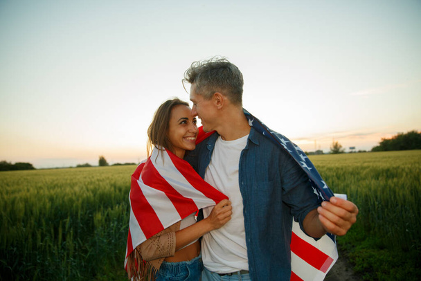 7月4日。7月4日。誇り高いカップルは日没の美しいランドマークに対して米国の旗を運ぶ。独立記念日、アメリカ国民の愛国的休日、民主主義と退役軍人の尊敬の概念 - 写真・画像