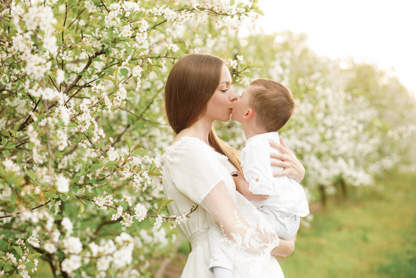 Portrait of happy mother and her baby boy. Beautiful touching scene of mom and son. Blooming garden in spring. - Photo, Image
