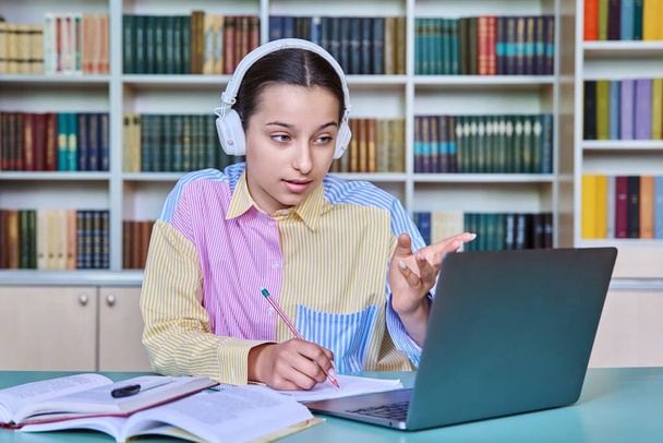 Teenage female student in headphones sitting in school library using laptop for video call conference chat looking at webcam. Online lesson, course, web seminar. Technology, e-learning, adolescence - Фото, зображення
