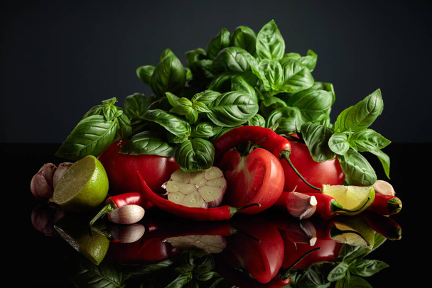 Ingredientes para hacer salsa de tomate. Tomates frescos, pimientos rojos, ajo, albahaca y lima sobre un fondo negro. - Foto, Imagen