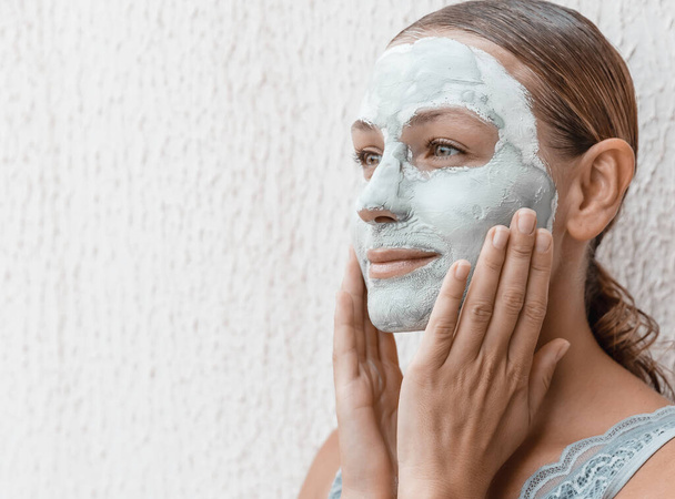 Portrait of a Beautiful Young Woman Applying Clay Mask Isolated on White Background. Enjoying Day Spa in Luxury Beauty Salon. - Фото, изображение