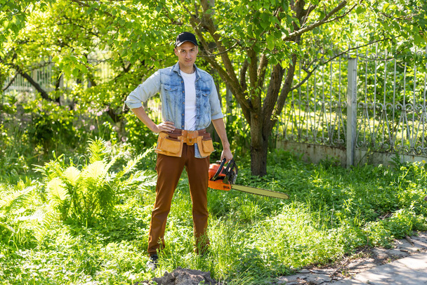 Ein Mann mit Kettensäge. entfernt Pflanzungen im Garten von alten Bäumen, erntet Brennholz - Foto, Bild