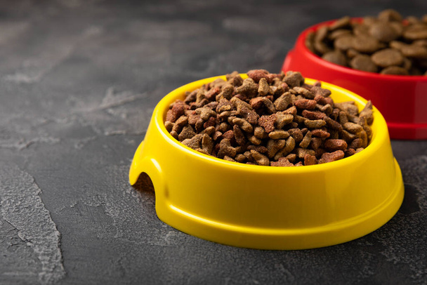 Dry food for cats and dogs in a yellow and red bowl on  cement background.Vitamins and nutrients for good health and pet energy. - Foto, Bild