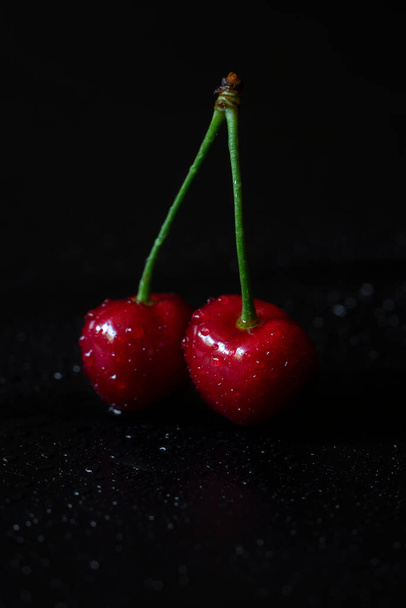 Close up photo of pair of fresh red cherries with water drops on black background. - Photo, Image