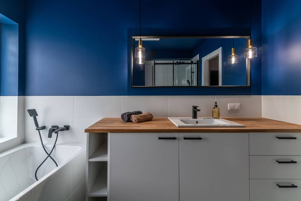 Modern bathroom with blue walls, white furniture and a bathtub - Фото, изображение