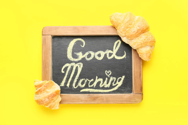 Chalkboard with text GOOD MORNING and tasty croissants on yellow background - Photo, Image