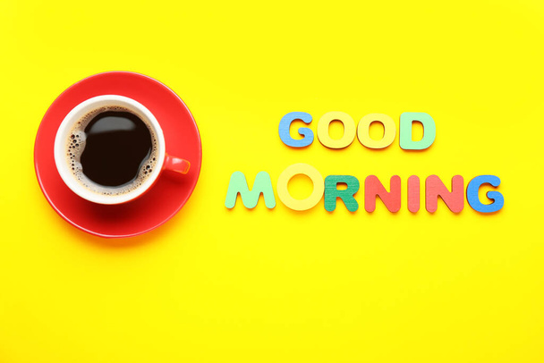 Text GOOD MORNING and cup of coffee on yellow background - Foto, imagen