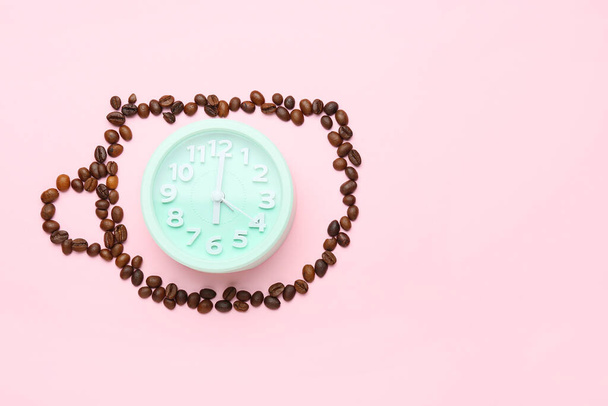 ピンクの背景にコーヒー豆と目覚まし時計で作られたカップ - 写真・画像