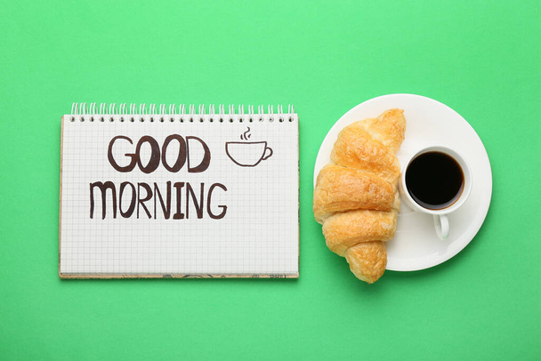 Cuaderno con texto Buenos días, taza de café y croissant sobre fondo verde - Foto, Imagen