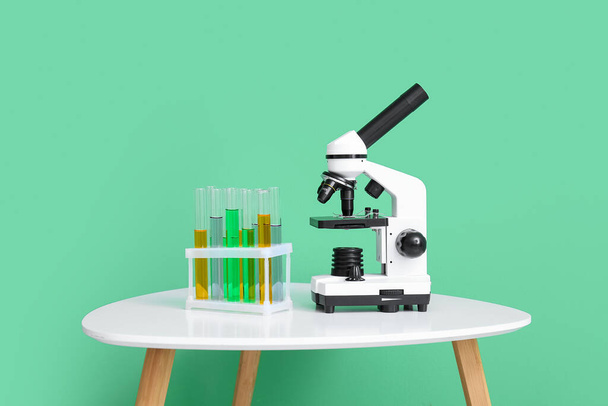 近代的な顕微鏡と緑の壁の近くのテーブルの上のサンプル試験管 - 写真・画像