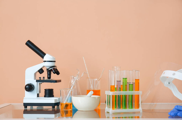 Microscopio moderno e vetreria da laboratorio con liquido sul tavolo vicino alla parete beige - Foto, immagini