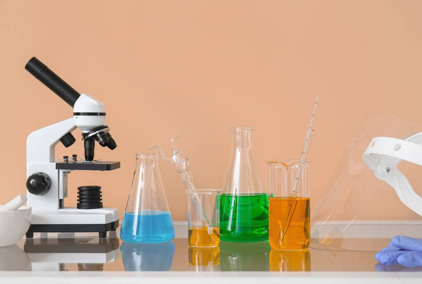 Microscope moderne et verrerie de laboratoire avec liquide sur la table près de la paroi beige - Photo, image