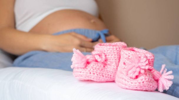 Дитяче взуття для вагітності. Красива вагітна жінка тримає рожеве дитяче взуття. Концепція вагітності, материнства, очікування народження дитини
 - Фото, зображення