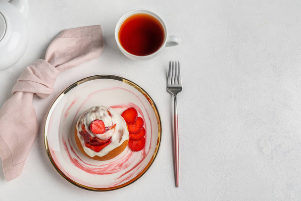 Placa con rollo de canela de fresa y taza de té sobre fondo blanco - Foto, imagen