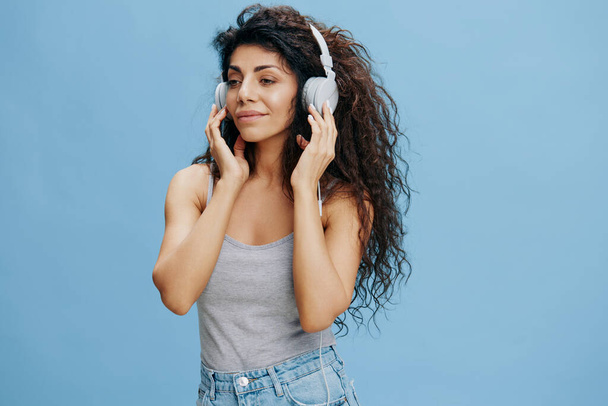 MUSIC AD CONCEPT in Verbindung setzen. Genießen Sie schöne lockige lateinamerikanische weibliche Touch-Kopfhörer, hören Lieblings-Playlist, entspannen. Cooles Angebot für Handy-PC-Zubehör, Karaoke. Studio schießen isoliert blauen Himmel Hintergrund - Foto, Bild