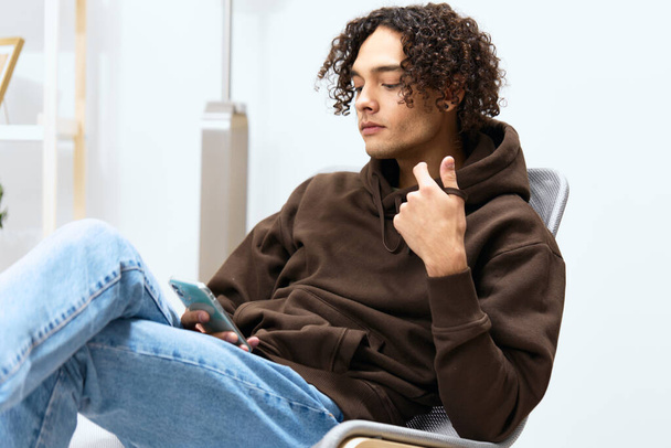 Um tipo com cabelo encaracolado sentado numa cadeira com tecnologias de telefone. Foto de alta qualidade - Foto, Imagem