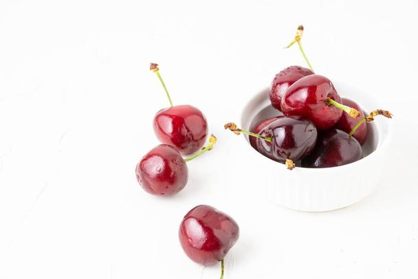 Top view of cherries in white bowl, selective focus, on white table, horizontal, with copy space - Photo, Image