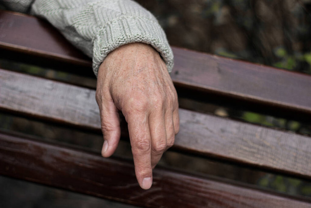 La solitaria mano mayor de un hombre. Un hombre mayor sentado en un banco, fondo bokeh, al aire libre - Foto, imagen