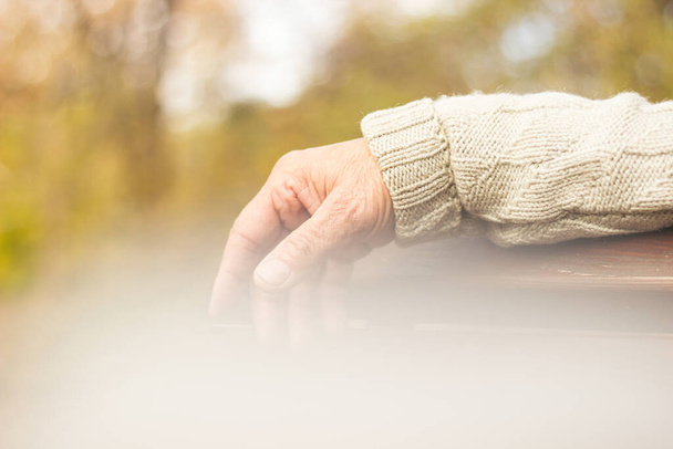 The lonely older hand of a man. An older man sitting on a bench, bokeh background, outdoors - Photo, Image