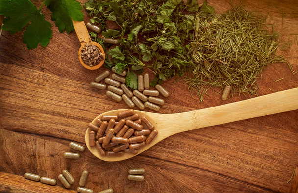 Grüne natürliche Kräutermedizin Kapsel Pille in Holzlöffeln auf Holz Tischhintergrund mit getrockneten Kräutern. Alternative Nahrungsmittel für einen gesunden Lebensstil. - Foto, Bild