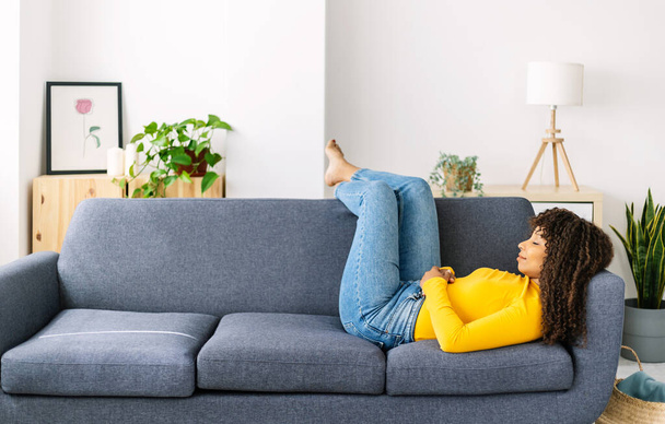 Junge Frau entspannt auf Sofa zu Hause - Müde Afroamerikanerin schläft auf Couch im Wohnzimmer - Foto, Bild