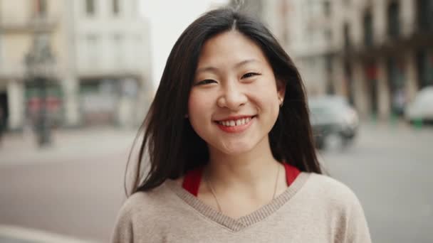 Muotokuva aasialaisesta naisesta katselemassa kameraa ja hymyilemässä kadulla. Onnellisia tunteita. Kaupunkielämän käsite - Materiaali, video